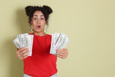 Shocked woman with dollar banknotes on pale green background, space for text