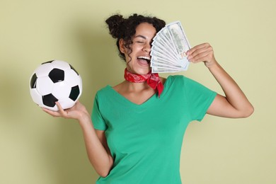 Happy woman with money and soccer ball on pale green background