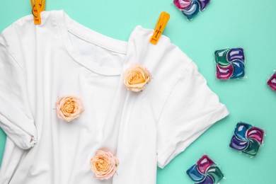 Photo of Laundry detergent pods, t-shirt, flowers and clothespins on turquoise background, flat lay