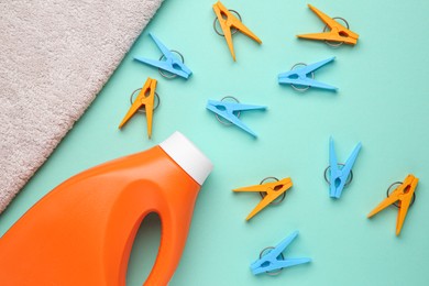 Bottle of laundry detergent, towel and many colorful clothespins on turquoise background, flat lay