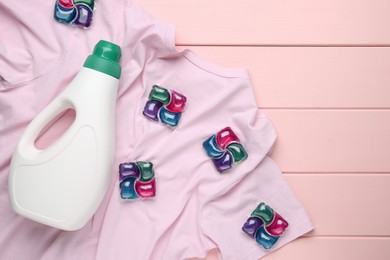 Photo of Laundry detergent in bottle, pods and t-shirt on pink wooden table, top view