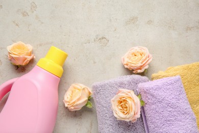 Photo of Laundry detergent in bottle, rose flowers and towels on grey textured table, flat lay. Space for text