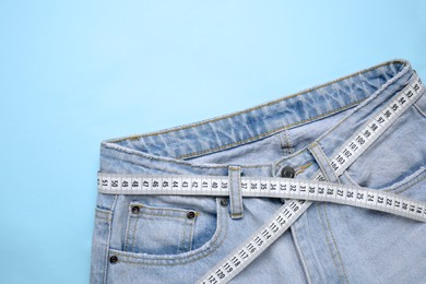 Photo of Jeans and measuring tape on light blue background, top view