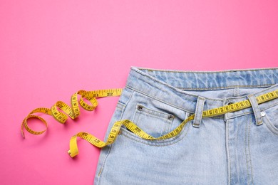 Photo of Jeans and measuring tape on pink background, top view