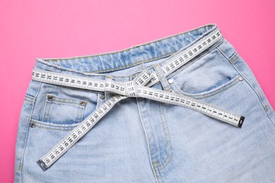 Photo of Jeans and measuring tape on pink background, top view