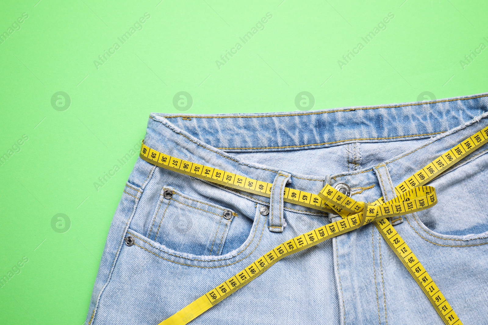 Photo of Jeans and measuring tape on green background, top view