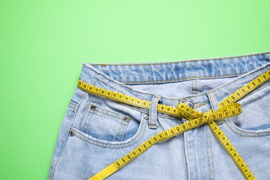 Photo of Jeans and measuring tape on green background, top view