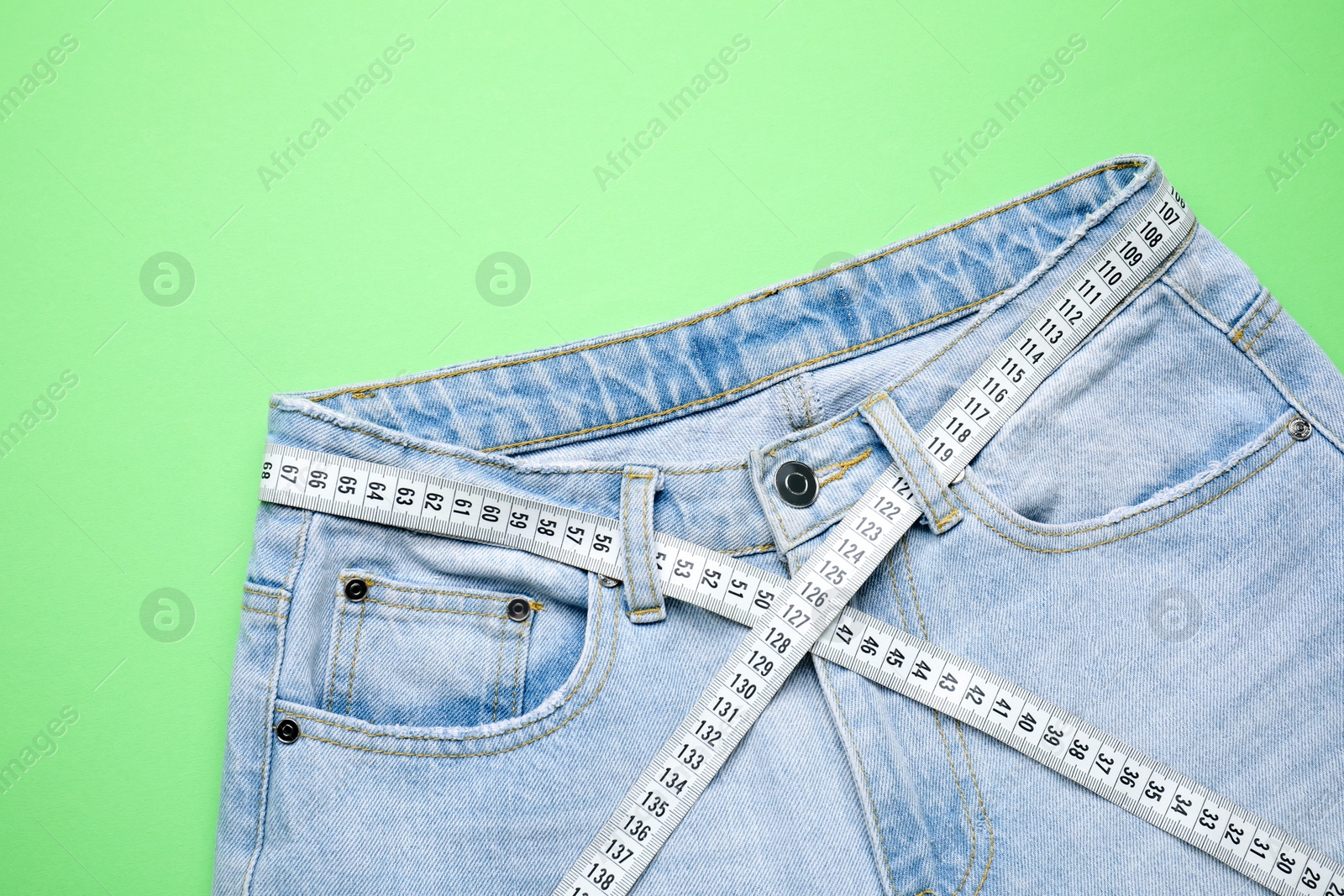 Photo of Jeans and measuring tape on green background, top view