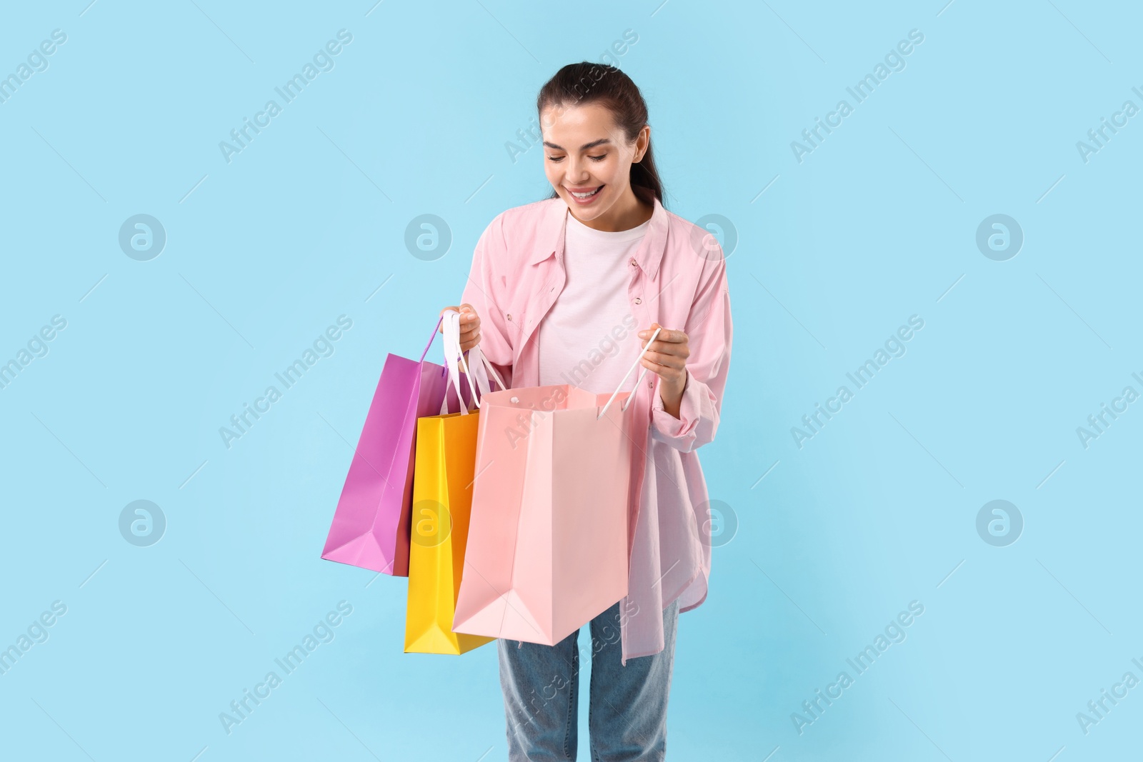 Photo of Happy woman looking into shopping bag on light blue background