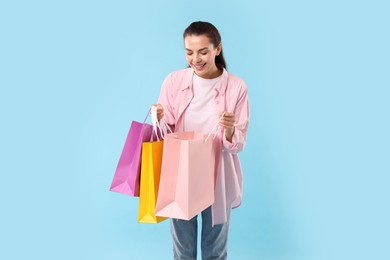 Happy woman looking into shopping bag on light blue background