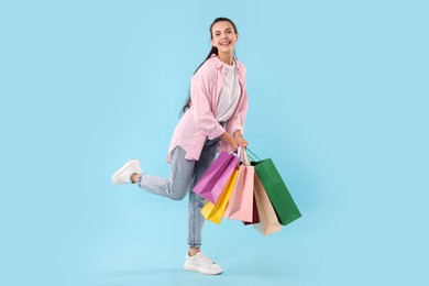 Smiling woman with colorful shopping bags on light blue background