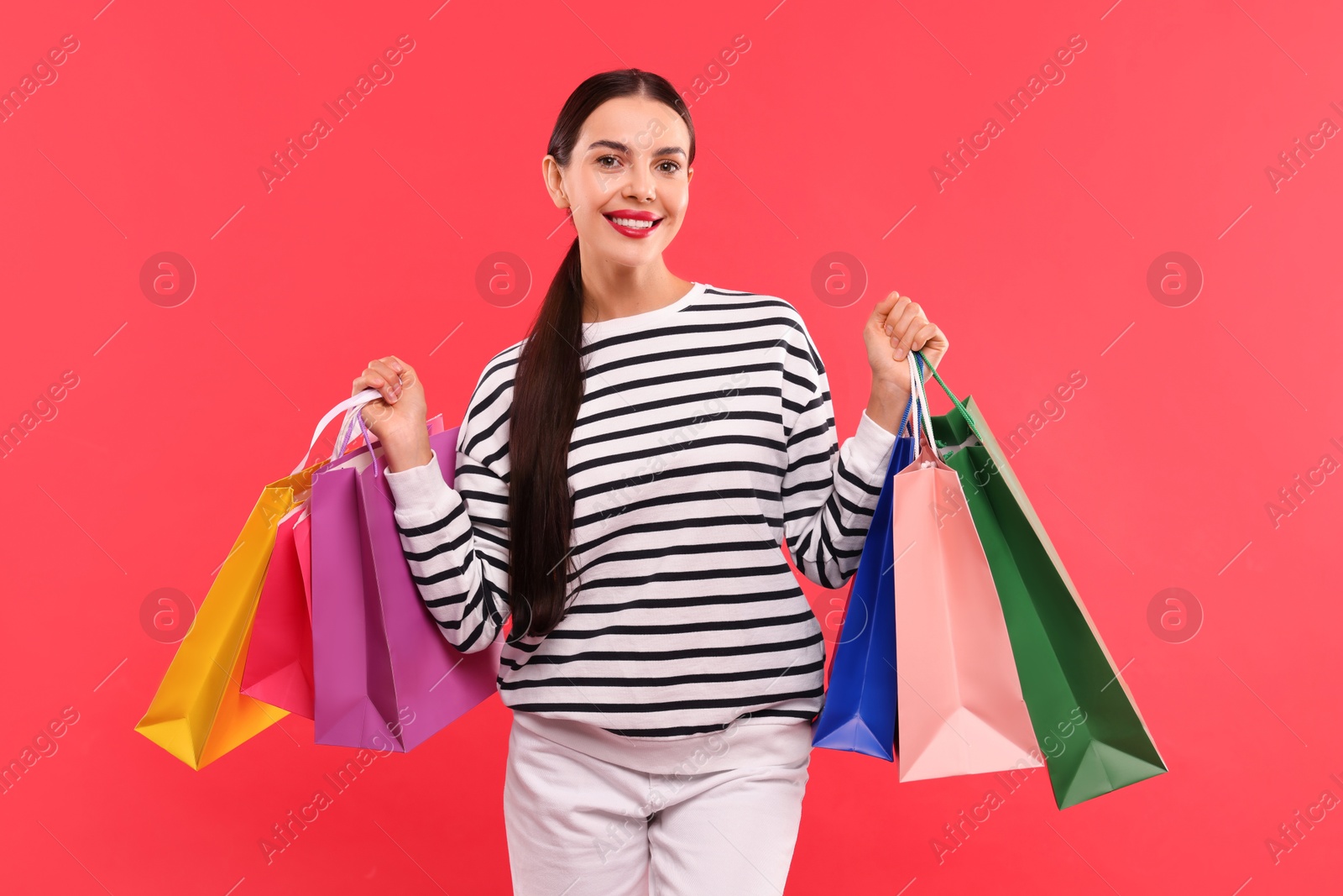 Photo of Smiling woman with colorful shopping bags on red background