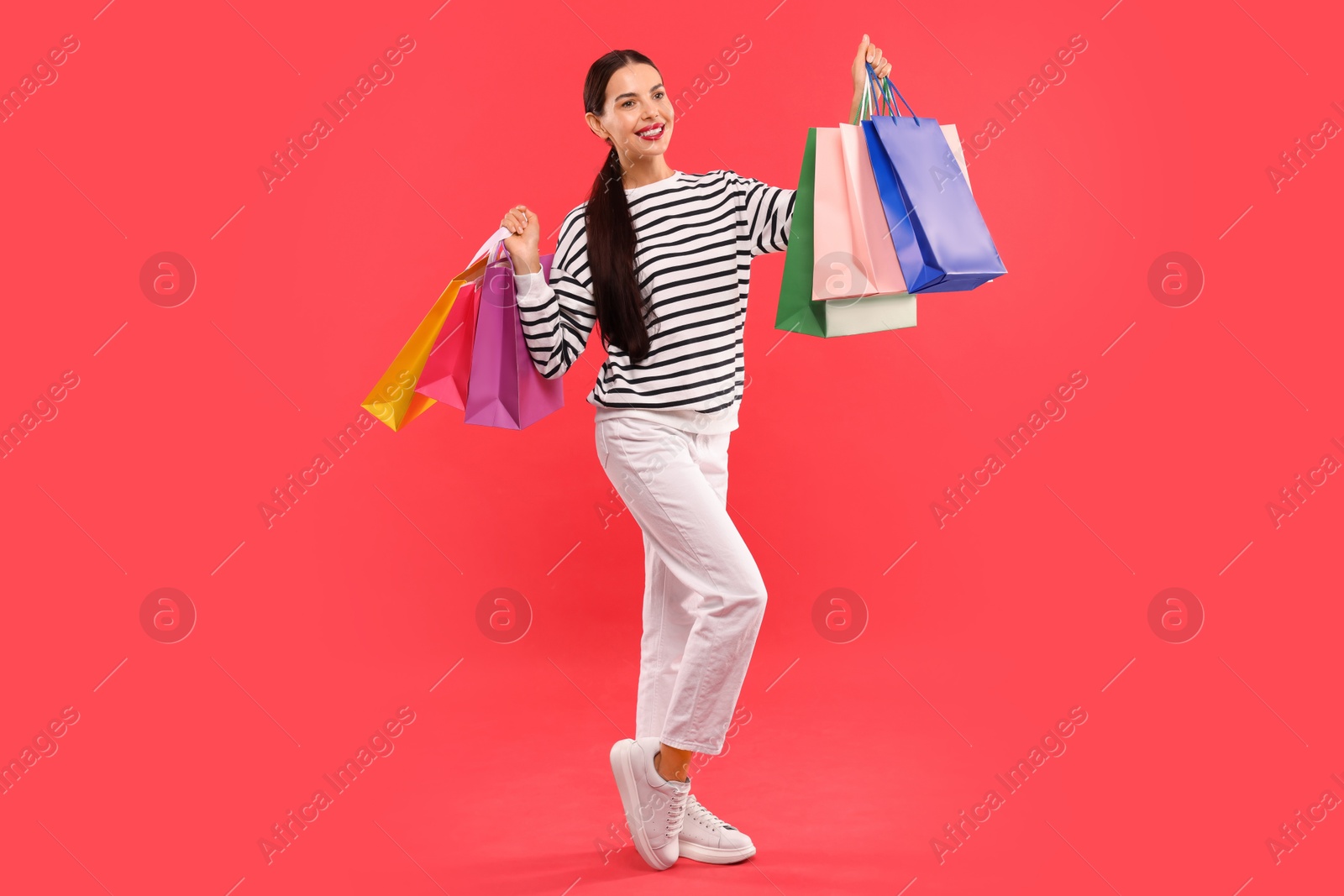 Photo of Smiling woman with colorful shopping bags on red background