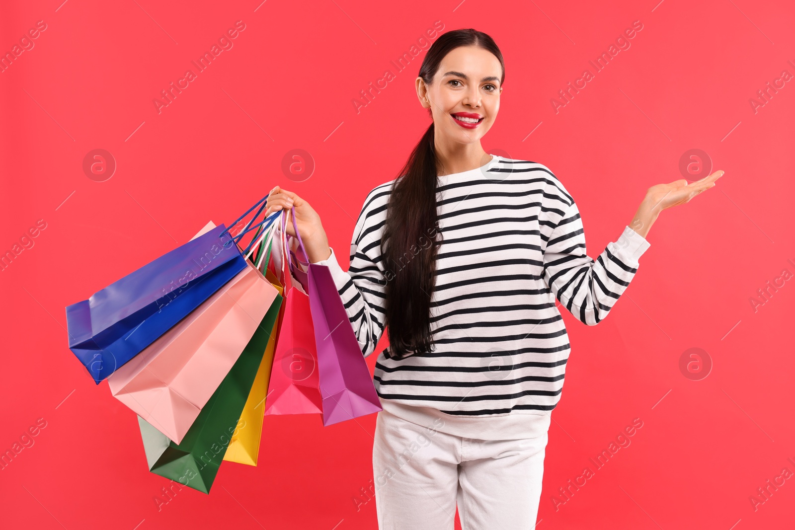 Photo of Smiling woman with colorful shopping bags holding something on red background