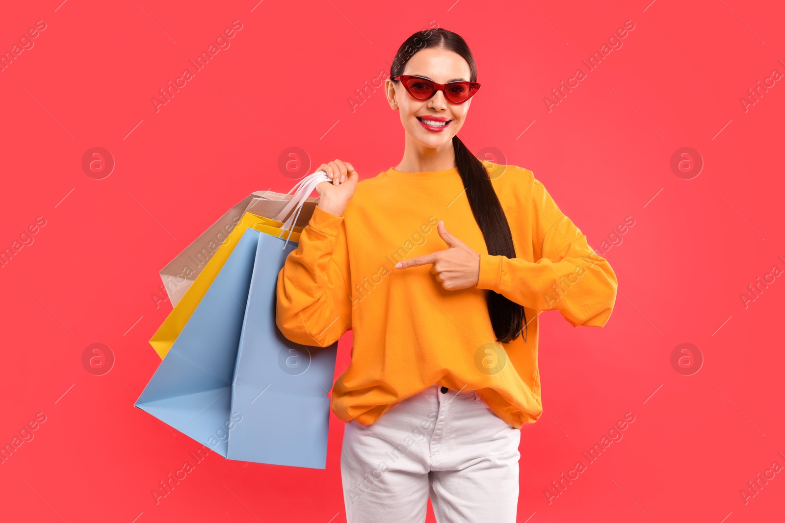 Photo of Smiling woman pointing at shopping bags on red background