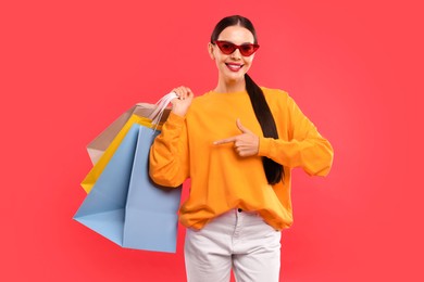 Smiling woman pointing at shopping bags on red background