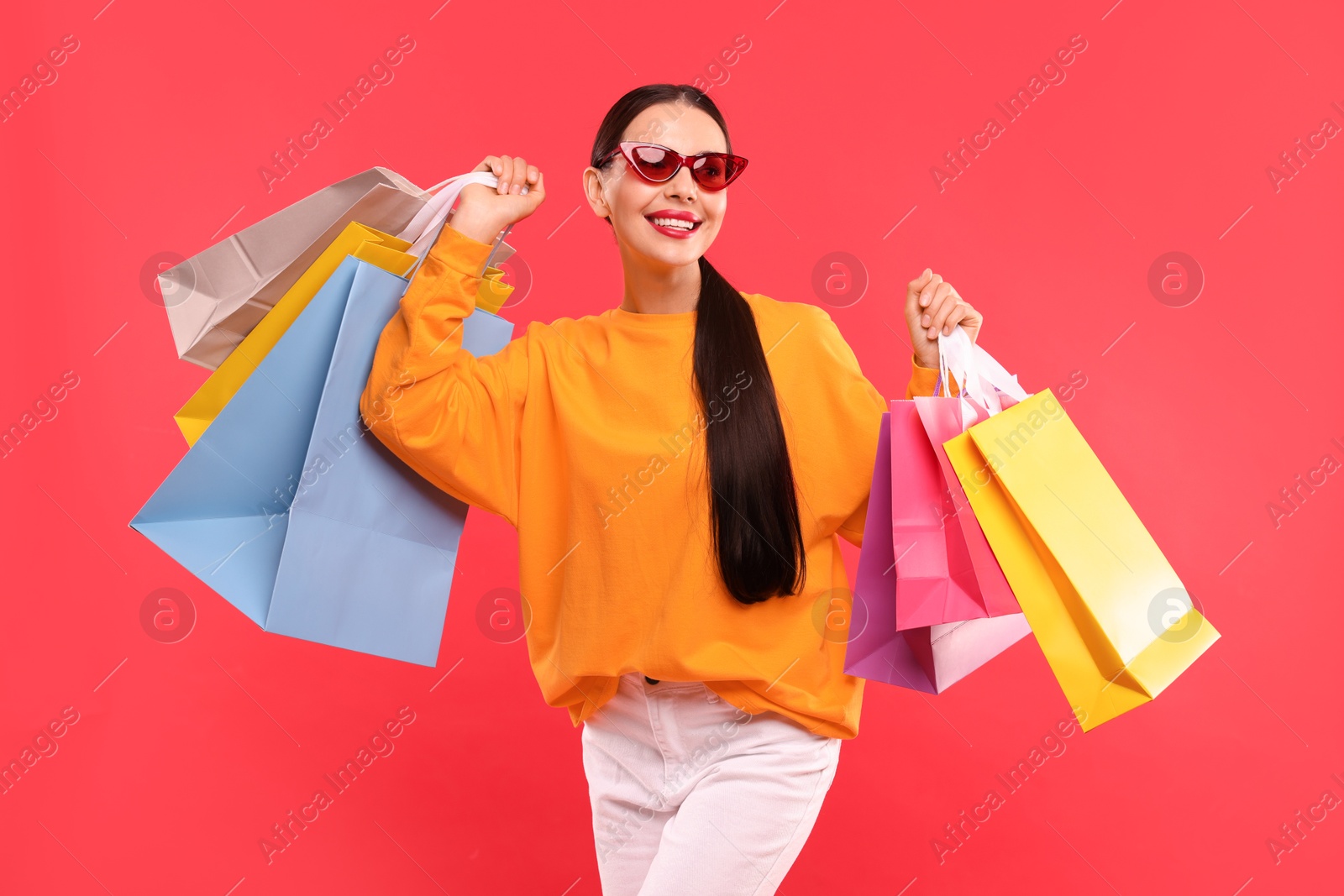 Photo of Smiling woman with colorful shopping bags on red background