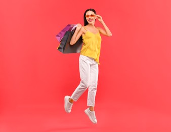 Smiling woman with colorful shopping bags jumping on red background