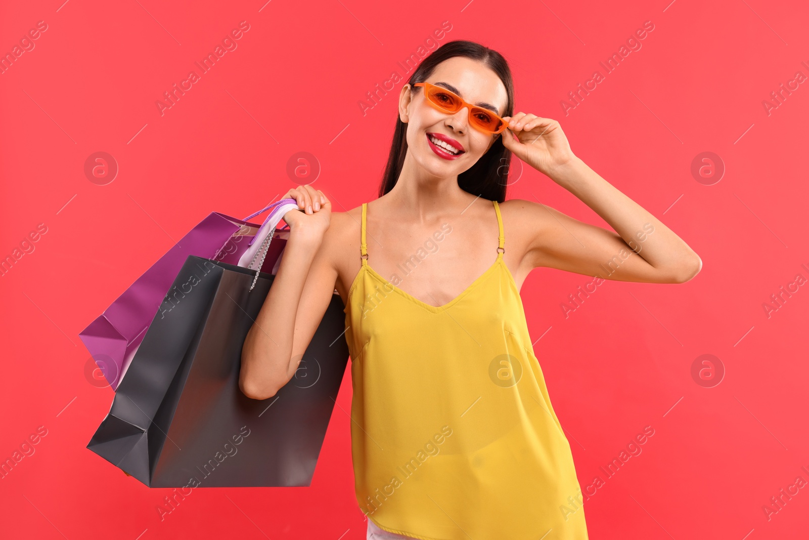 Photo of Smiling woman with colorful shopping bags on red background