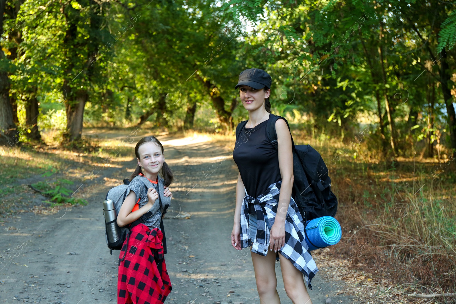 Photo of Portrait of smiling mother and daughter with backpacks travelling in beautiful forest