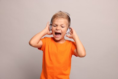 Little boy listening to music on light grey background