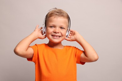 Little boy listening to music on light grey background