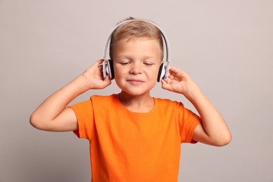 Little boy listening to music on light grey background