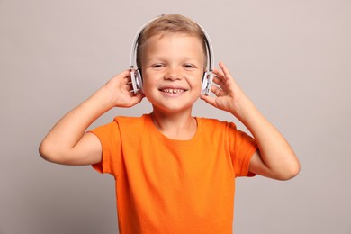 Little boy listening to music on light grey background