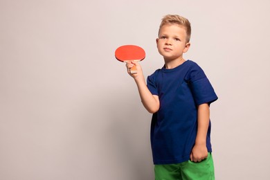 Little boy with ping pong racket on light grey background, space for text