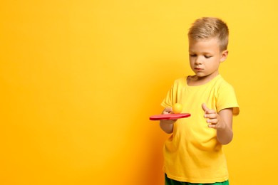 Little boy with ping pong racket and ball on orange background, space for text