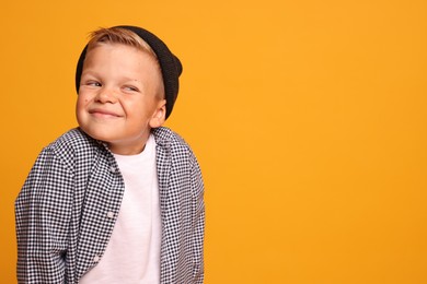 Portrait of little boy with stylish clothes on orange background, space for text