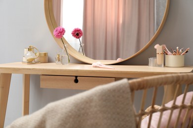 Dressing table with mirror, cosmetic products and flower indoors. Interior design