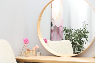 Dressing table with mirror, cosmetic products and flower indoors. Interior design