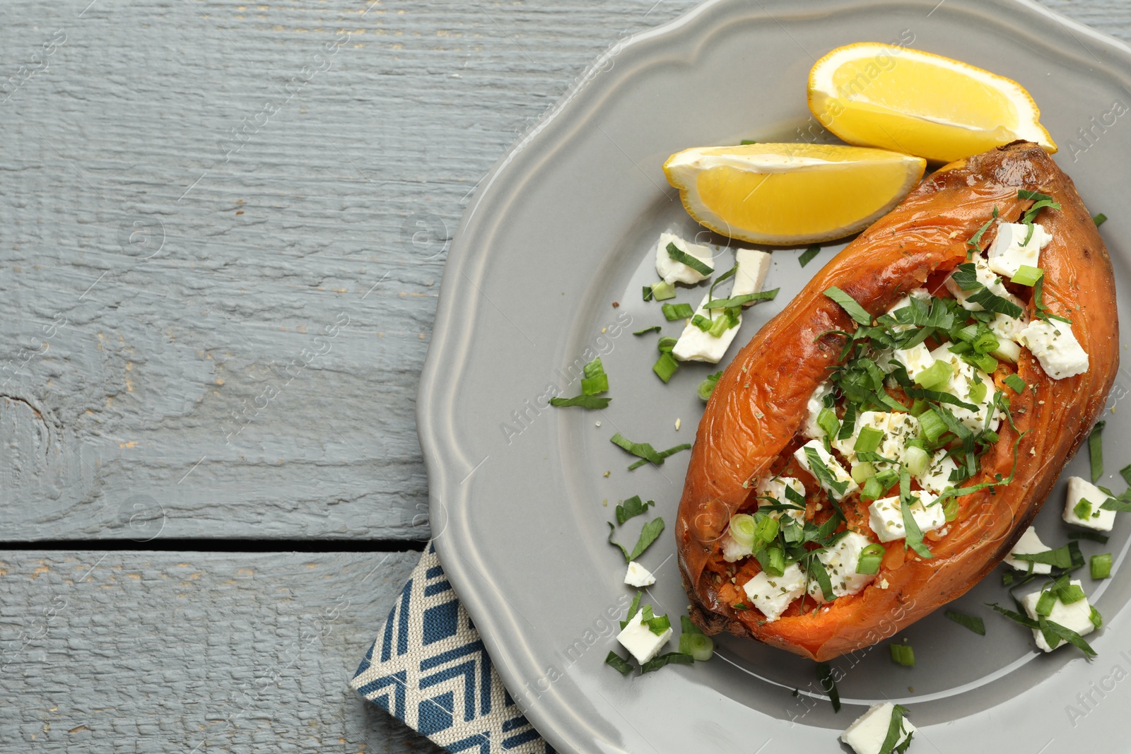 Photo of Tasty cooked sweet potato with feta cheese, lemon and green onion on grey wooden table, top view. Space for text