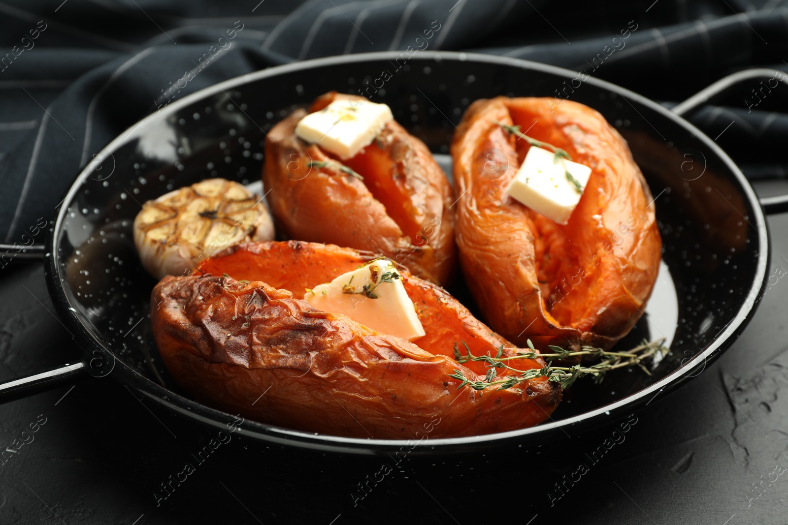 Photo of Tasty cooked sweet potatoes with feta cheese, garlic and thyme on black table, closeup