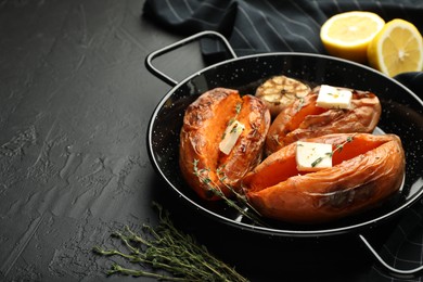 Photo of Tasty cooked sweet potatoes with feta cheese, garlic, thyme and lemon on black table, closeup. Space for text