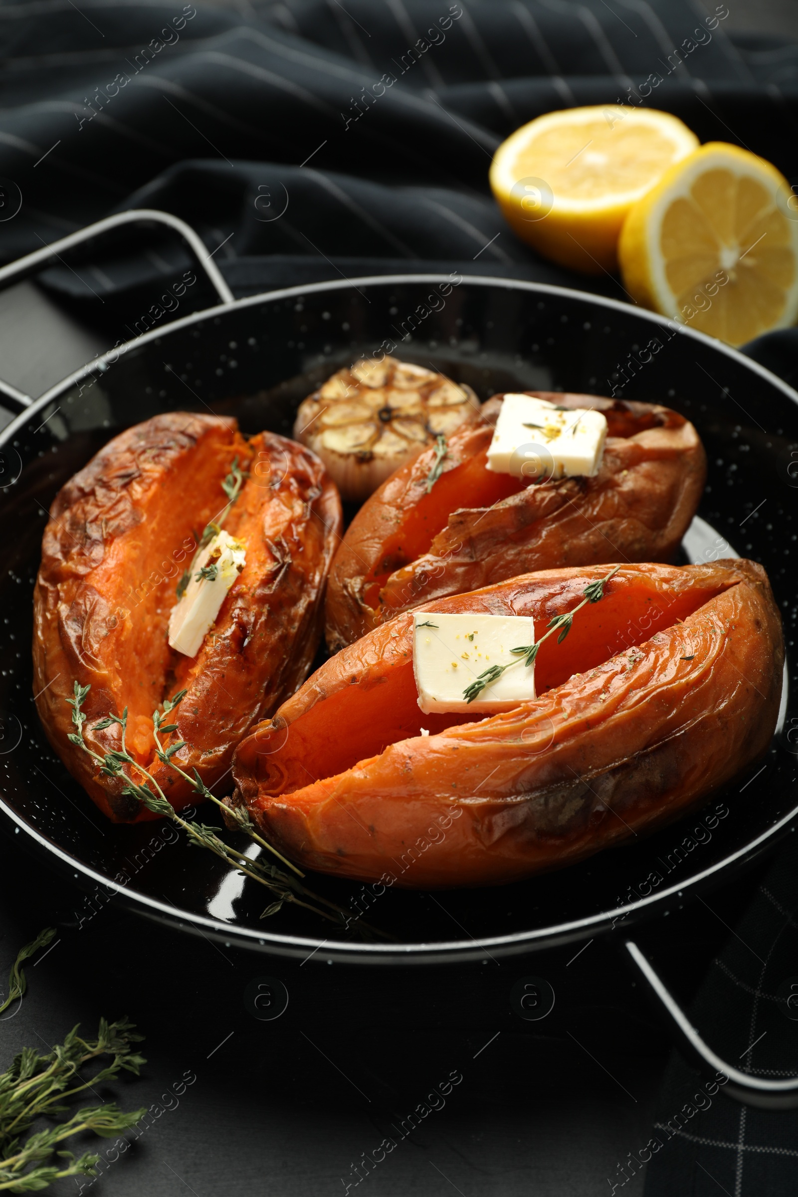 Photo of Tasty cooked sweet potatoes with feta cheese, garlic, thyme and lemon on black table, closeup