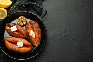 Photo of Tasty cooked sweet potatoes with feta cheese, garlic, thyme and lemon on black table, top view. Space for text