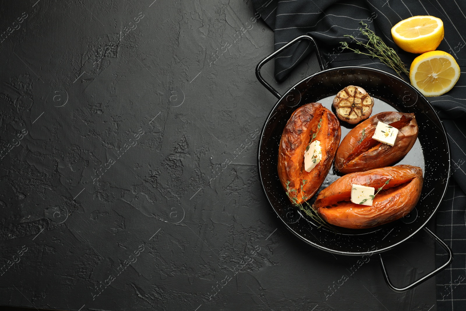 Photo of Tasty cooked sweet potatoes with feta cheese, garlic, thyme and lemon on black table, top view. Space for text