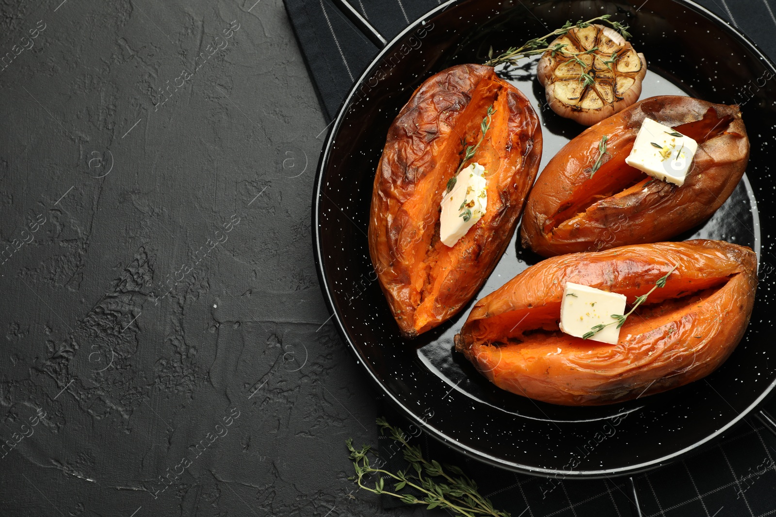 Photo of Tasty cooked sweet potatoes with feta cheese, garlic and thyme on black table, top view. Space for text