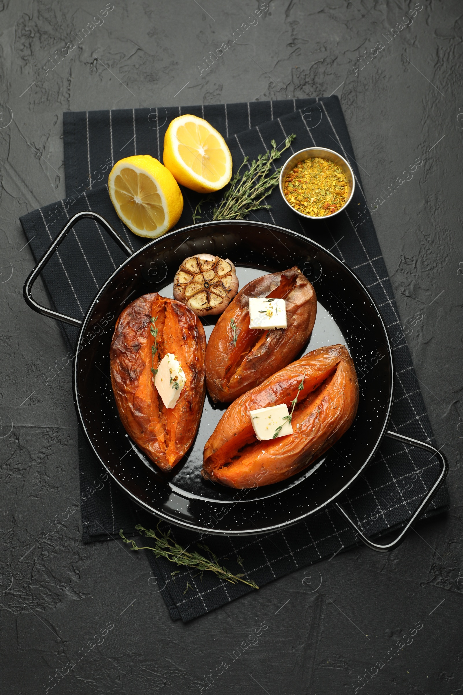 Photo of Tasty cooked sweet potatoes with feta cheese, garlic, thyme and lemon on black table, top view