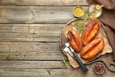 Photo of Tasty cooked sweet potatoes with rosemary on wooden table, top view. Space for text