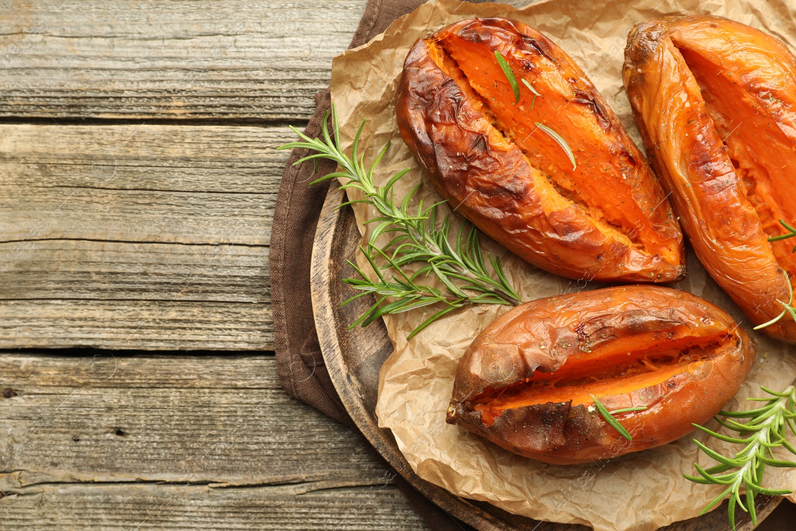 Photo of Tasty cooked sweet potatoes with rosemary on wooden table, top view. Space for text