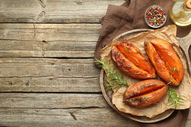 Tasty cooked sweet potatoes with rosemary on wooden table, top view. Space for text