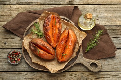 Tasty cooked sweet potatoes with rosemary on wooden table, top view