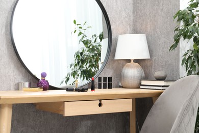 Photo of Mirror, dressing table with cosmetic products, lamp, chair and houseplant indoors. Interior design