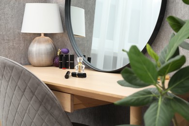 Dressing table with mirror, cosmetic products, houseplant and chair indoors. Interior design