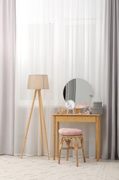 Mirror, dressing table, lamp and stool near window indoors. Interior design