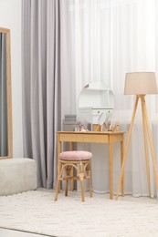 Mirror, dressing table, lamp and stool near window indoors. Interior design