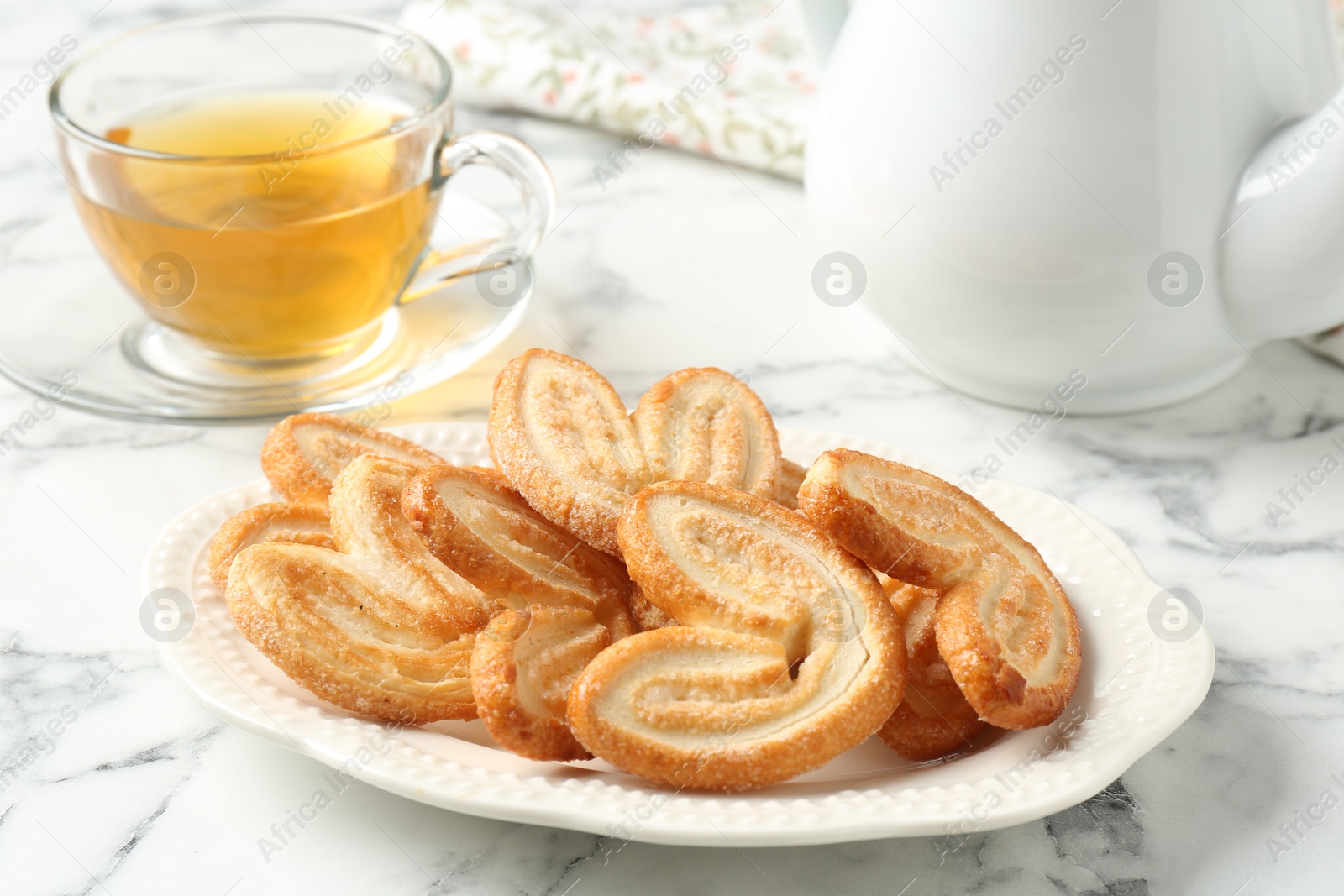 Photo of Delicious palmier cookies with tea on white marble table, closeup